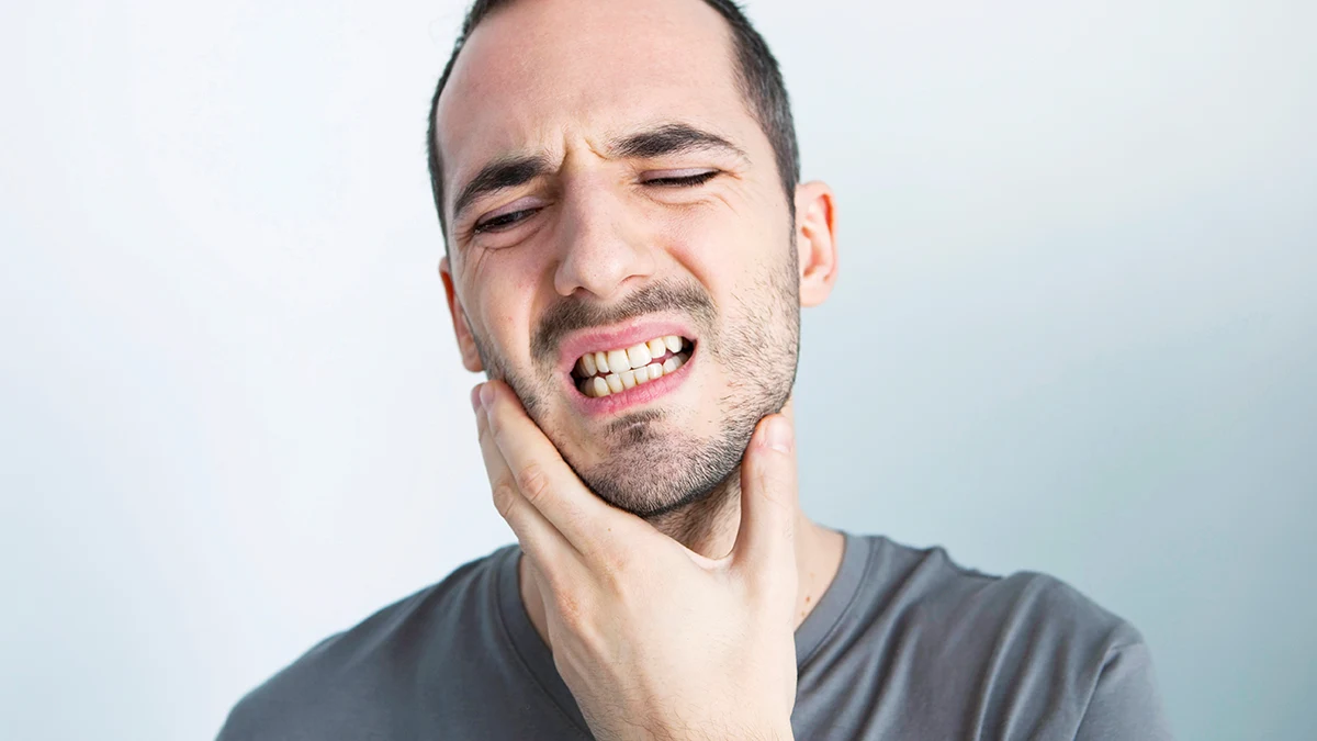 hombre sosteniendo su mandíbula debido al dolor de bruxismo